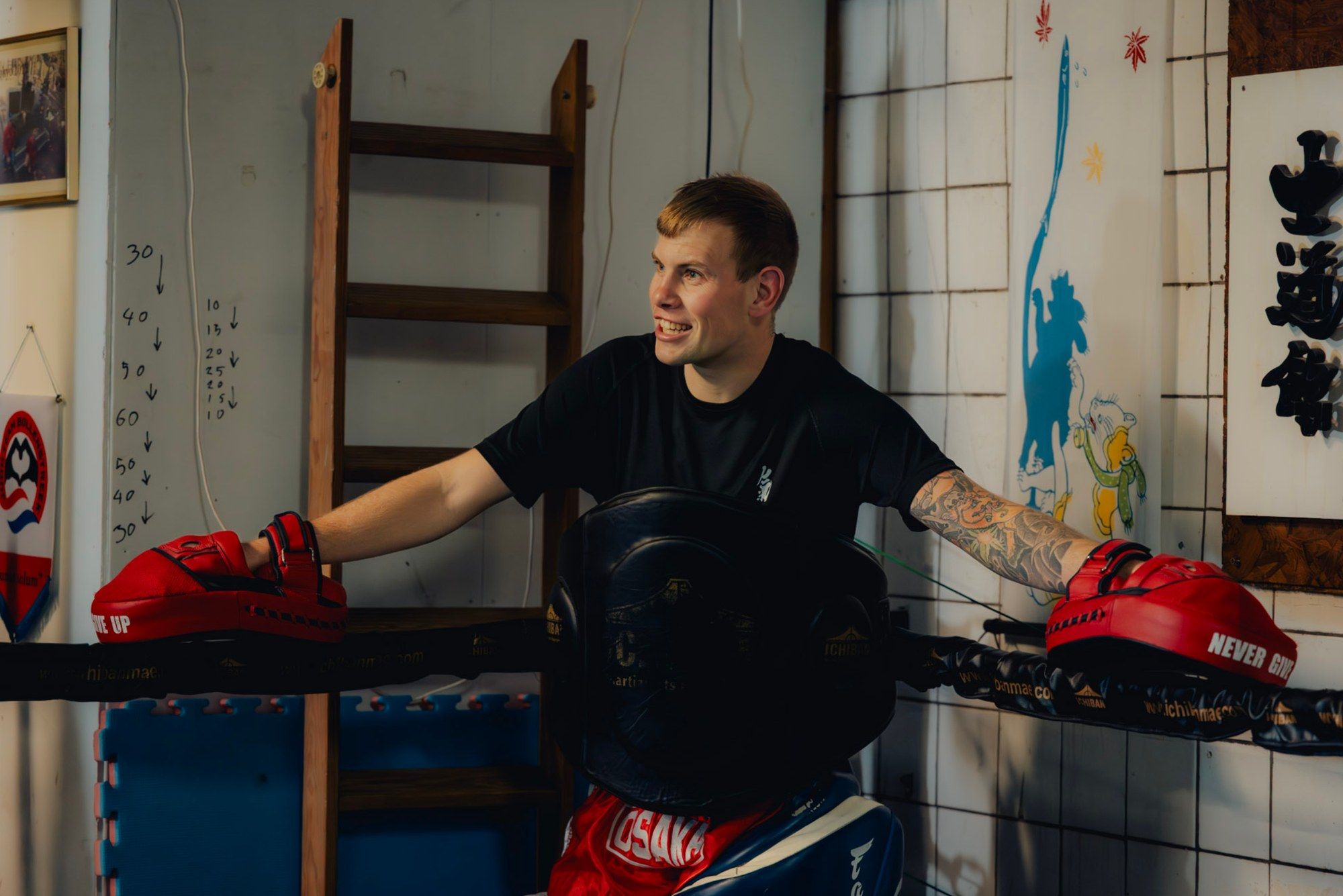 Floris lacht, leunend tegen de touwen van de ring, met pads in beide handen.