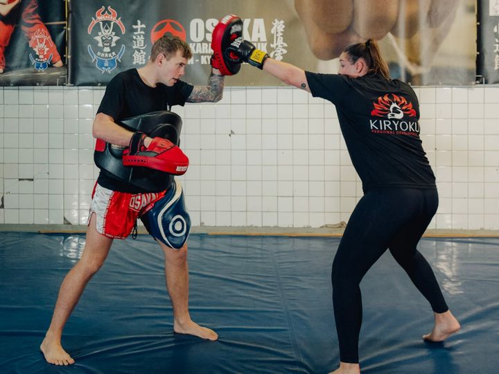 Een klant in een Kiryoku-shirt stoot op de pad die Floris vasthoudt, in de dojo van Osaka Karate Katwijk.