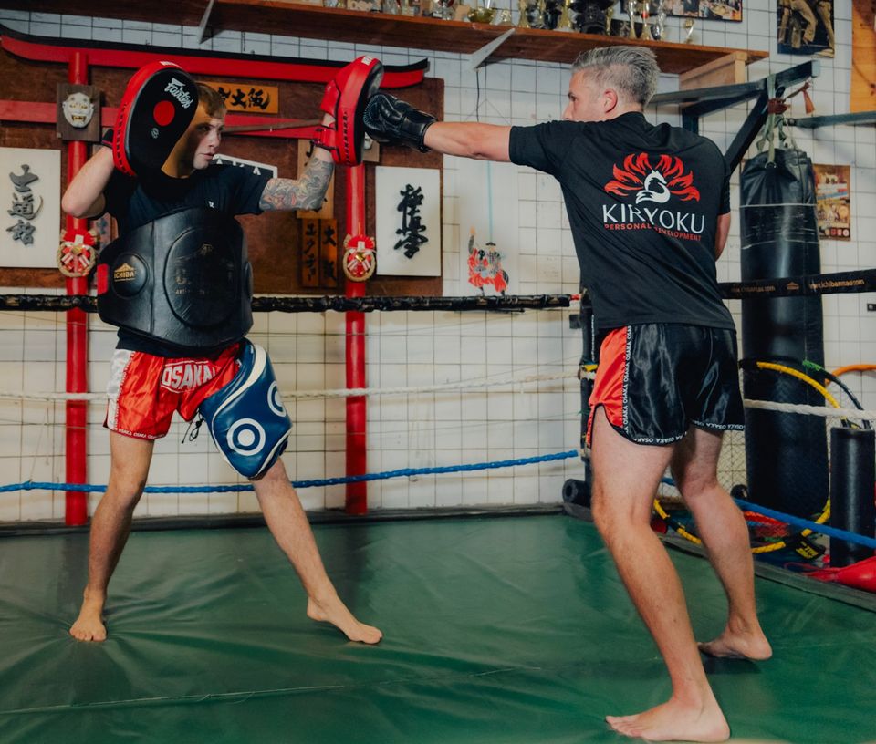 Floris houdt pads vast terwijl een klant in een Kiryoku-shirt stoot, in de ring van de dojo.