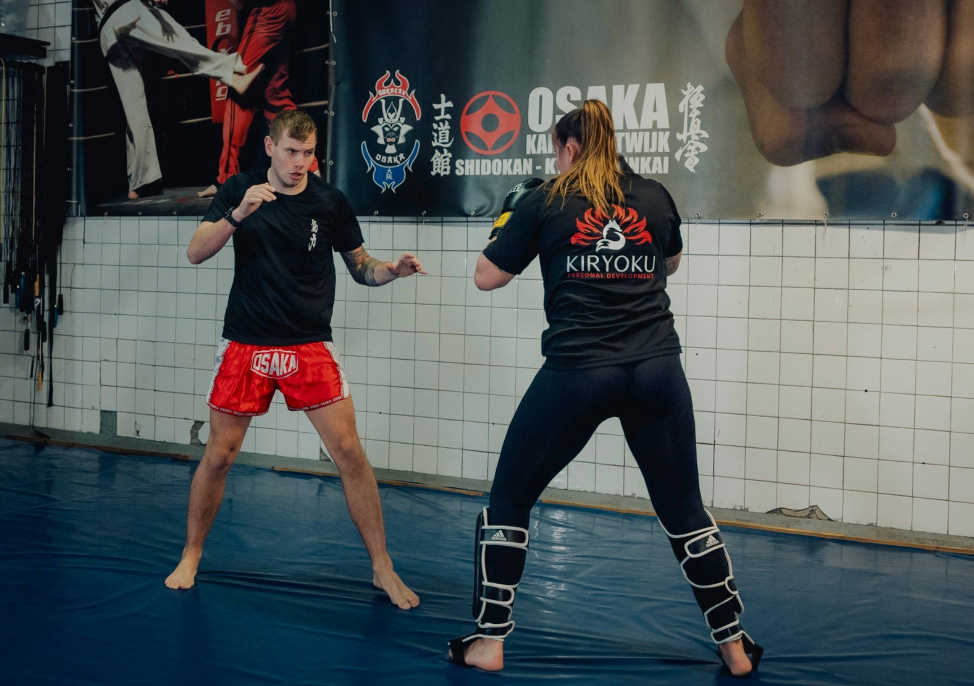 Floris en een klant staan tegenover elkaar in gevechtshouding, onder de banner van Osaka Karate Katwijk.