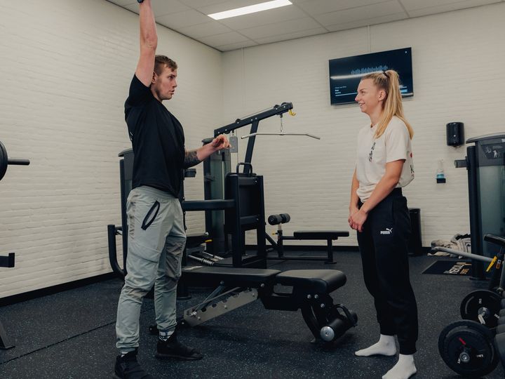 Floris corrigeert een klant die een dumbbell boven haar hoofd drukt.