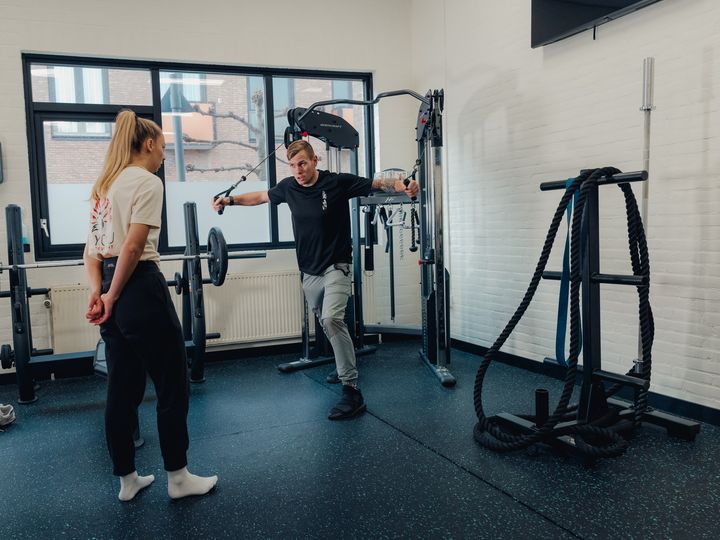 Floris doet een kabeltrek-oefening voor aan een klant in een lichte gym.